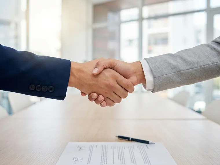 Aperto de mãos entre dois profissionais sobre um contrato assinado